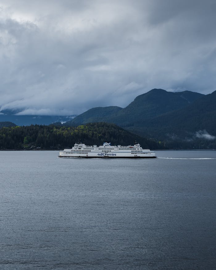 A serene view of a BC Ferries vessel traversing calm waters, set against a backdrop of mountains and fog.