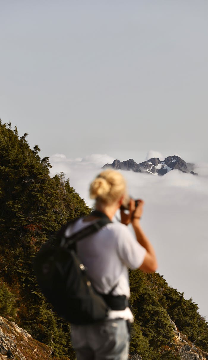 A photographer stands on a cliff in BC, Canada, capturing stunning mountain views above the clouds.